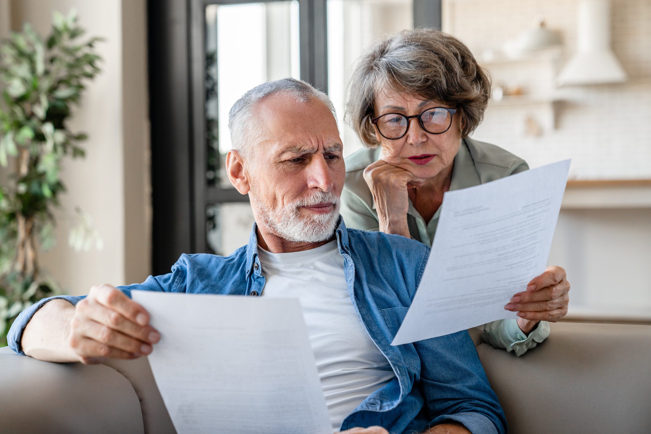 Elderly couple reviewing documents on couch.
